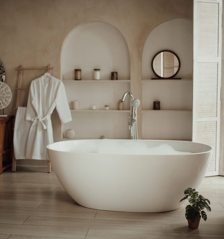 Soft native hues organic shapes look of bathroom with big window oval bathtub in neutrals tones. Green palm plants candles bubblebath leasure and relaxation skin selfcare wellness luxury living